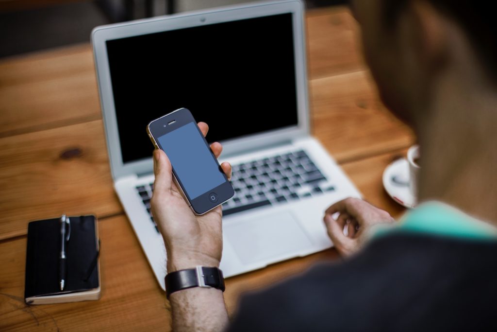 person with phone in front of computer